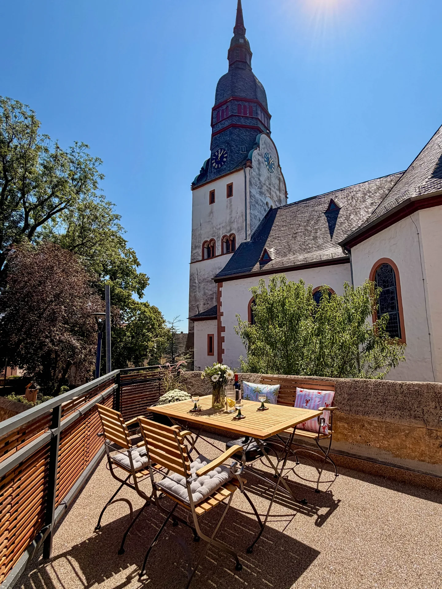 Sonniger Balkon des Markt Quartiers in Nierstein mit Sitzgruppe und Blick auf die benachbarte Kirche.
