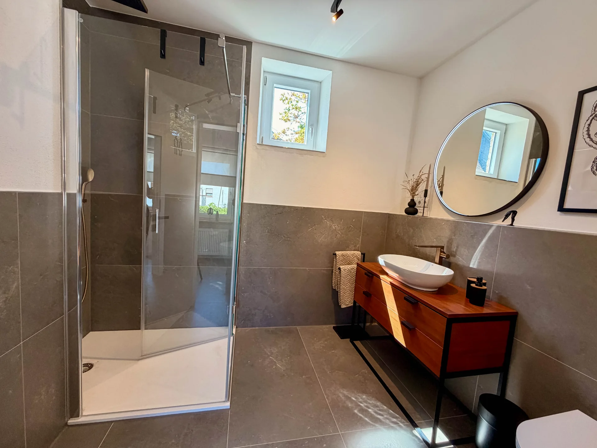 Modernes Badezimmer des Markt Quartiers mit Dusche, Aufsatzwaschbecken und rundem Spiegel.