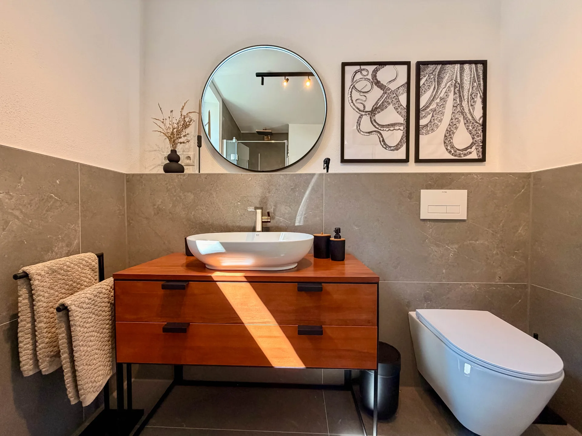 Modernes Badezimmer des Markt Quartiers mit Dusche, Aufsatzwaschbecken und rundem Spiegel.